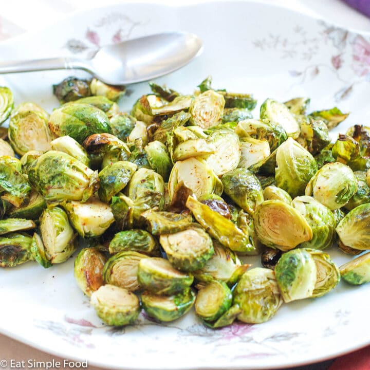 Brown Roasted Brussels Sprouts, cut in half, and on a white plate with pink roses on the edge and a silver spoon.
