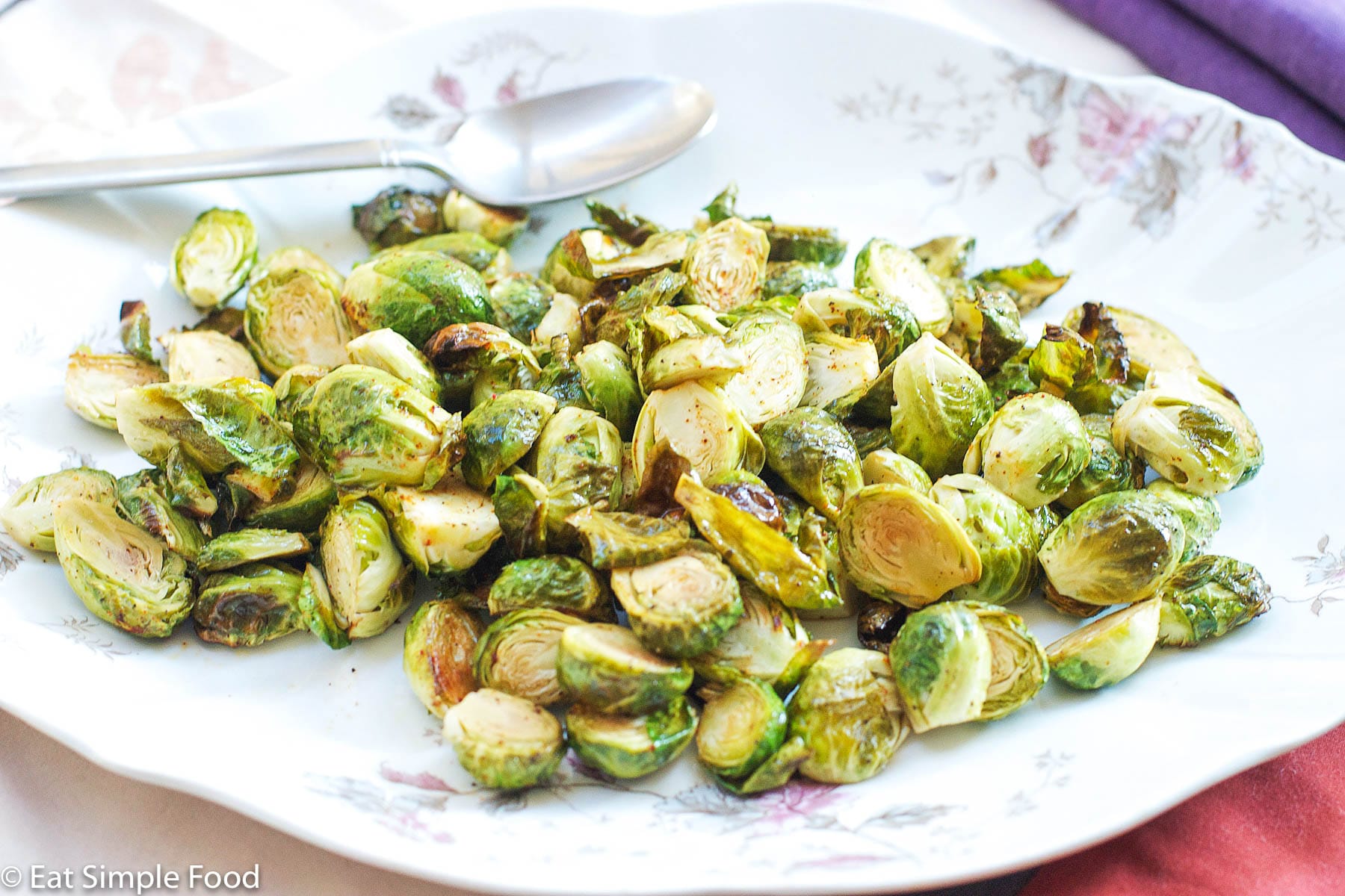 Brown Roasted Brussels Sprouts, cut in half, and on a white plate with pink roses on the edge and a silver spoon.