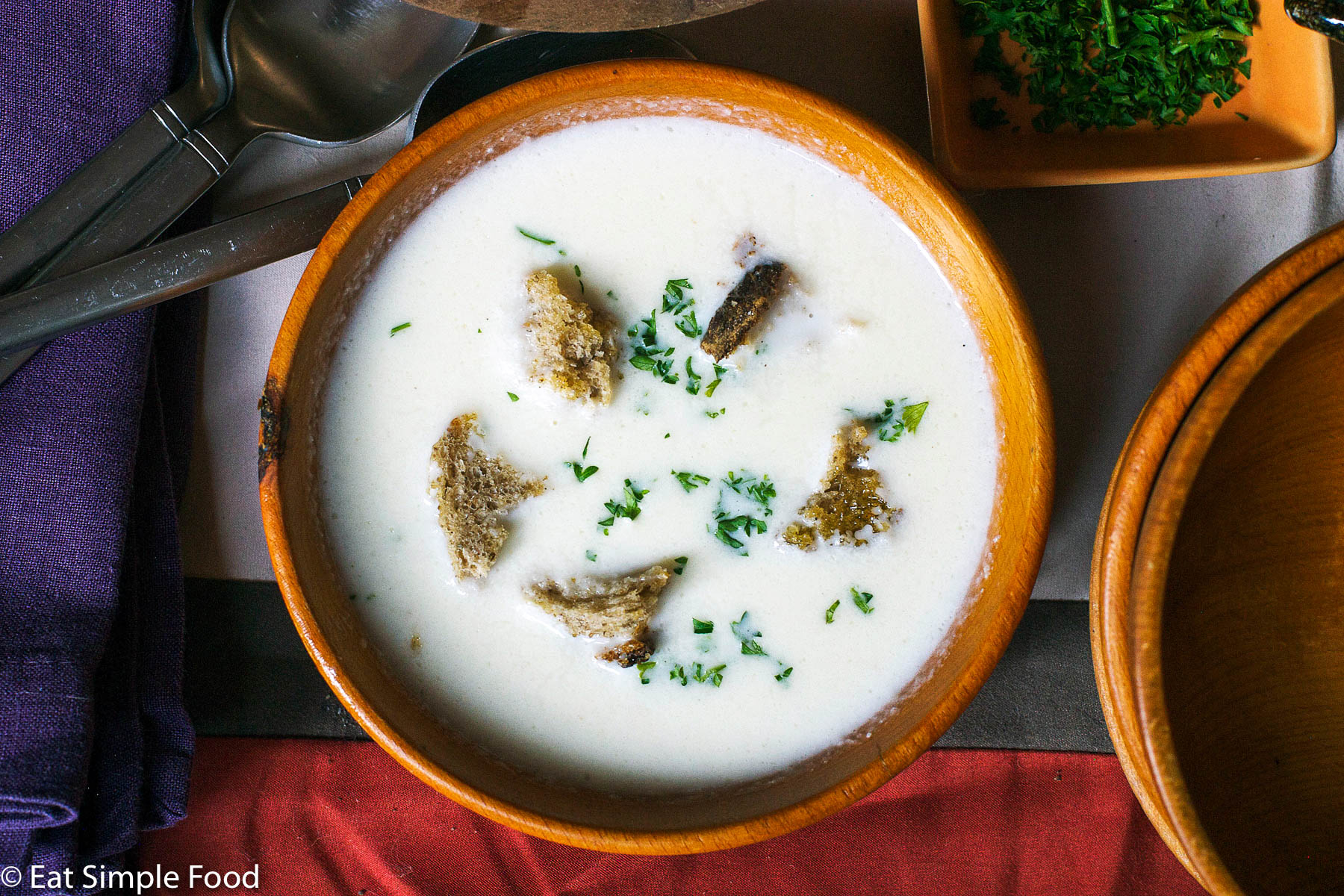 Top View wood bowl of white cauliflower soup with 5 croutons and a chopped parsley garnish