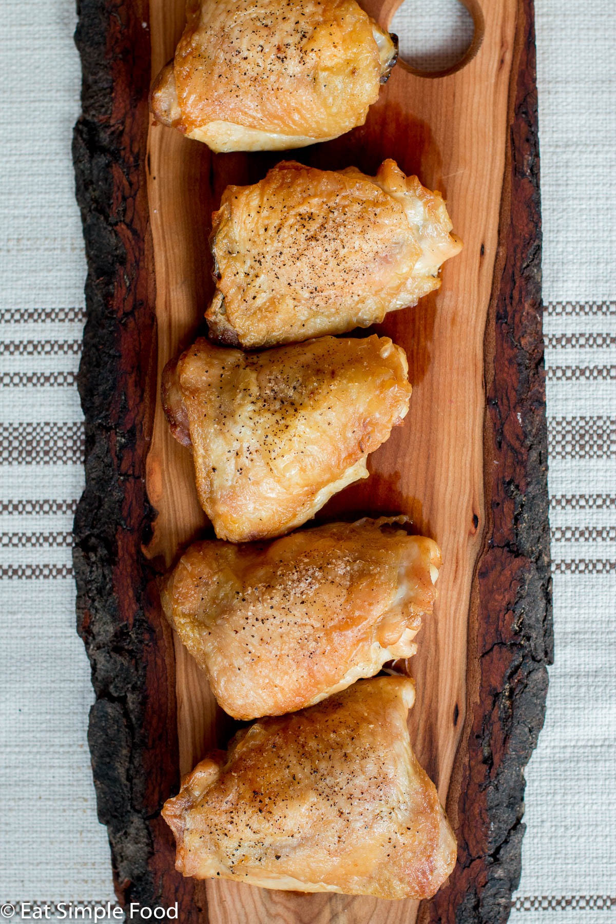 Top view. 5 Roasted bone in skin on chicken thighs on a live edge wood cutting board