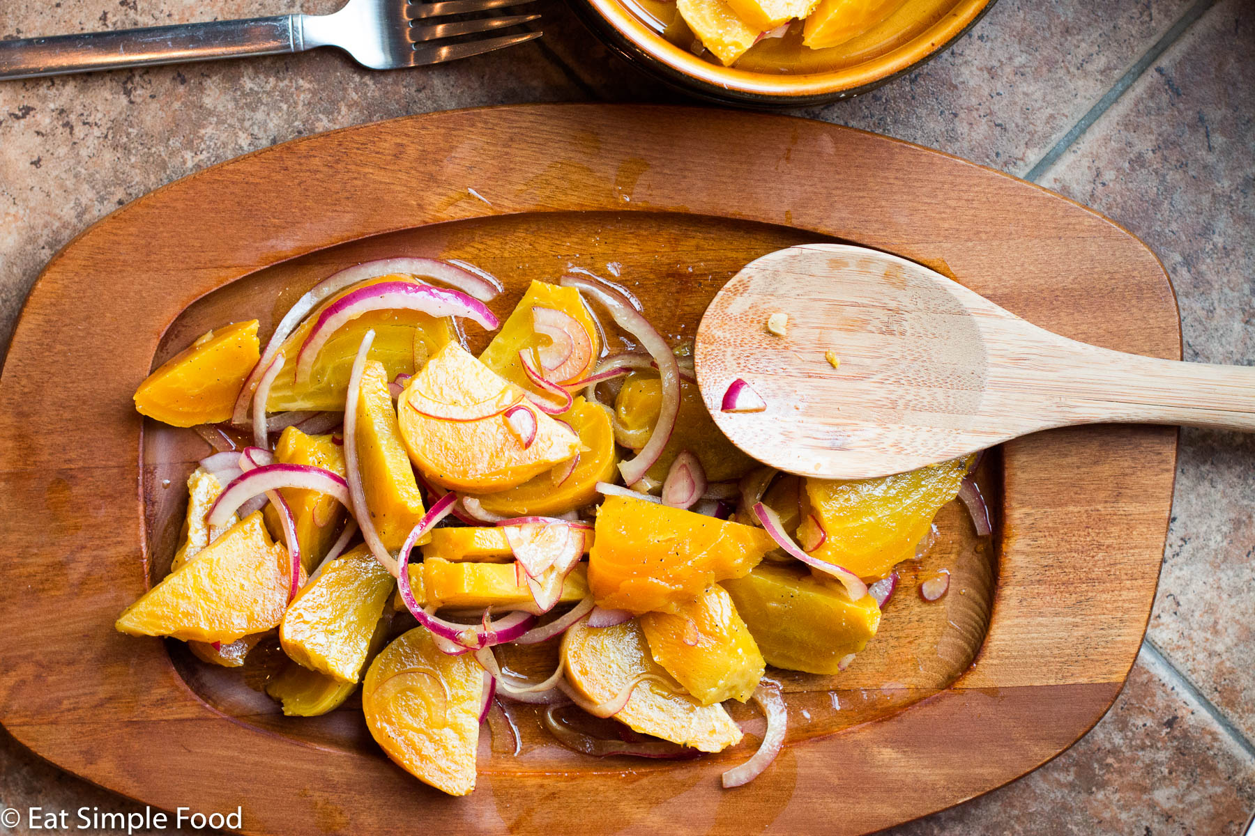 Yellow Golden Beets roasted and sliced and tossed with red onions and a dressing. On a wood plate with a wood spoon.