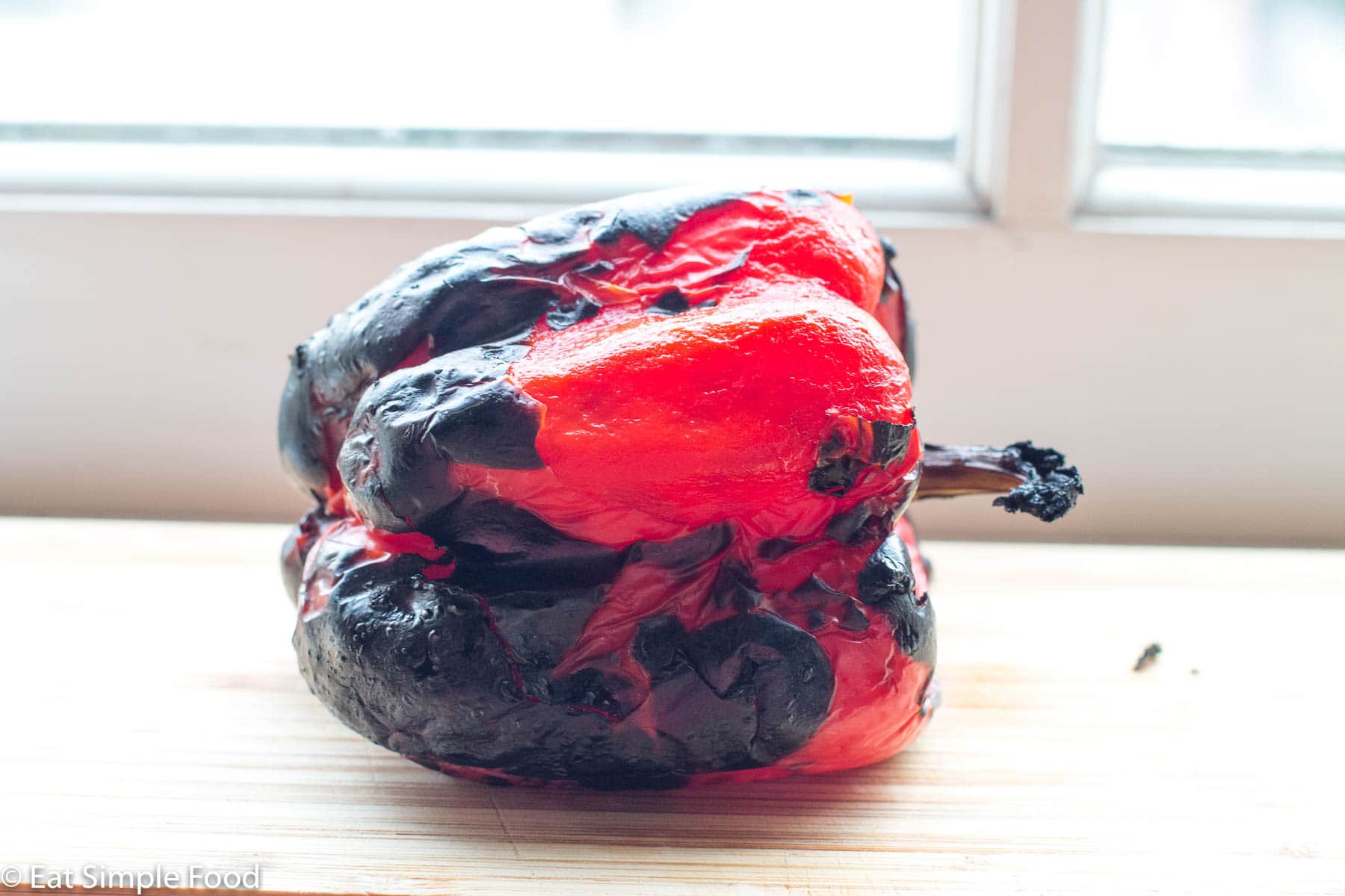 Roasted black Red Pepper sitting on a wood cutting board by a window.