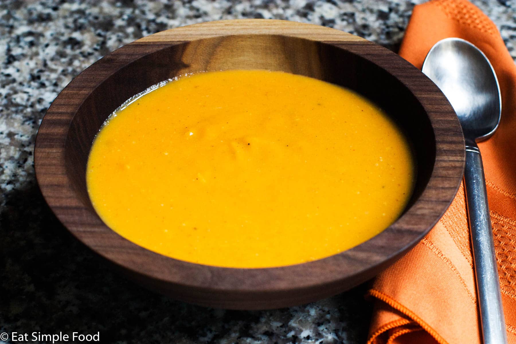 Creamy Orange sweet potato soup in a wood bowl with a spoon on the side and an orange napkin.