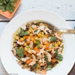 Top view of ¾ white deep plate with wild rice, chunks of roast sweet potatoes and chickpeas. Topped with cilantro and toasted coconut flakes.