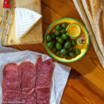 Sliced Salami, Brie Cheese, Baguette Loaf and bowl of olives,