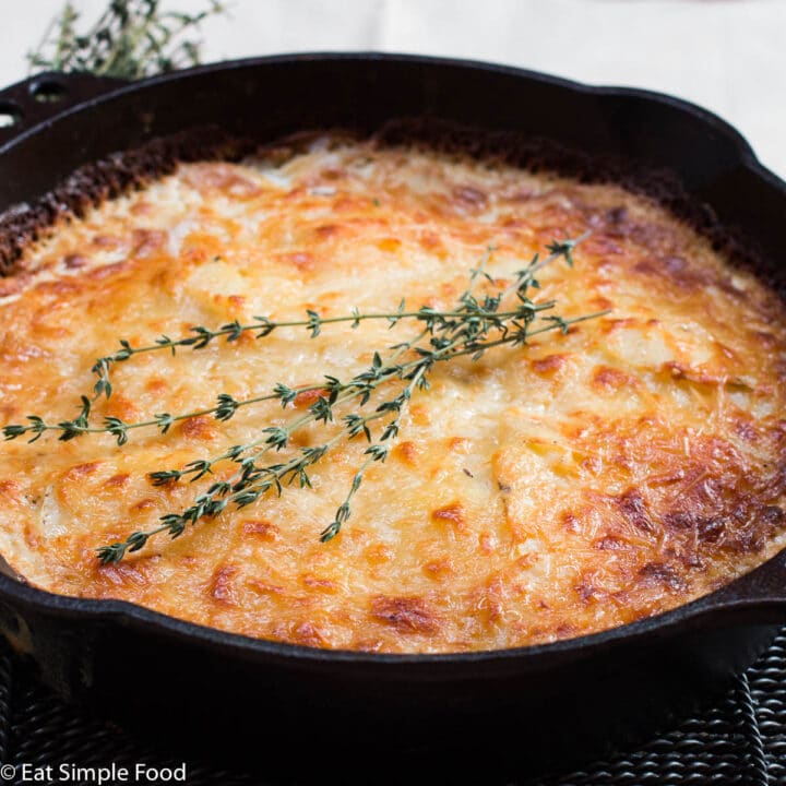 Scalloped Potatoes Cooked Golden Brown in Cast Iron Skillet with Thyme garnish.