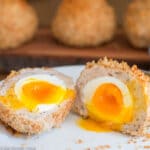 Cooked Soft boiled Egg Wrapped in Turkey, Coated With Panko, Baked And Cut In half on a plate.