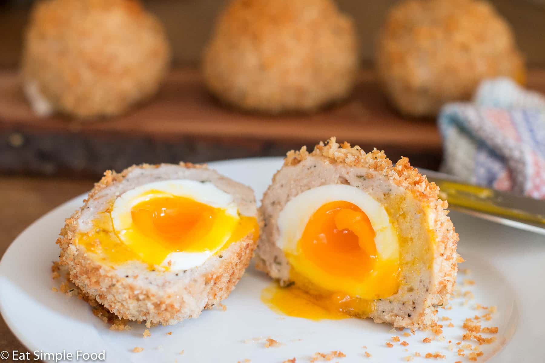 Cooked Soft boiled Egg Wrapped in Turkey, Coated With Panko, Baked And Cut In half on a plate.