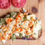 Top View Of Toast with Mashed Avocado, Scrambled Egg, and Hot Sauce On a Cutting Board with tomato Slices