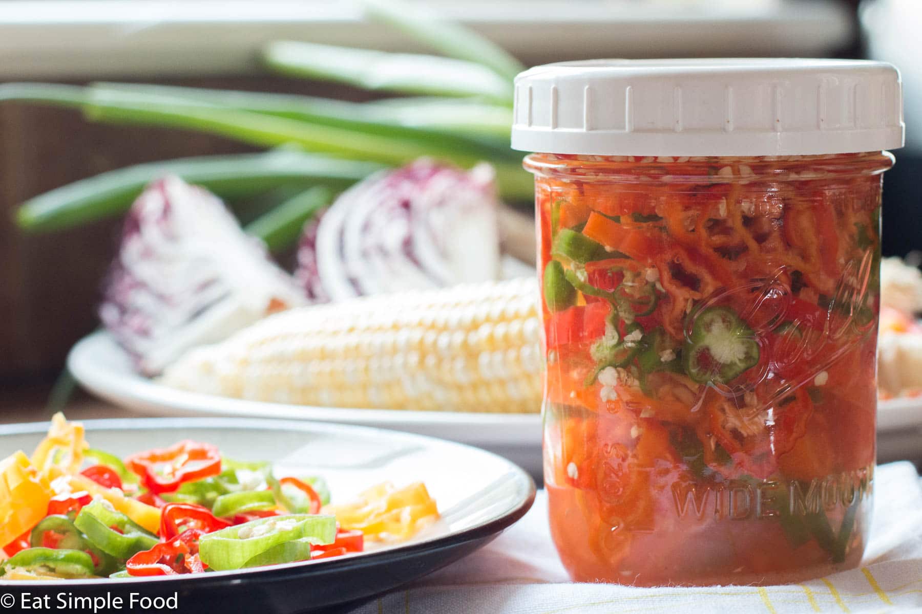 Mason Jar with White Lid of Preserved Sliced Red, Orange, & Yellow Shishito Peppers