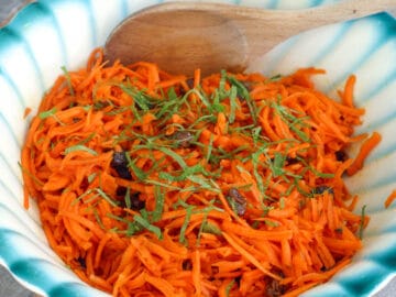 Grated Carrots, Raisins, toasted Walnuts, and sliced Mint Salad in a white bowl with a blue rim.