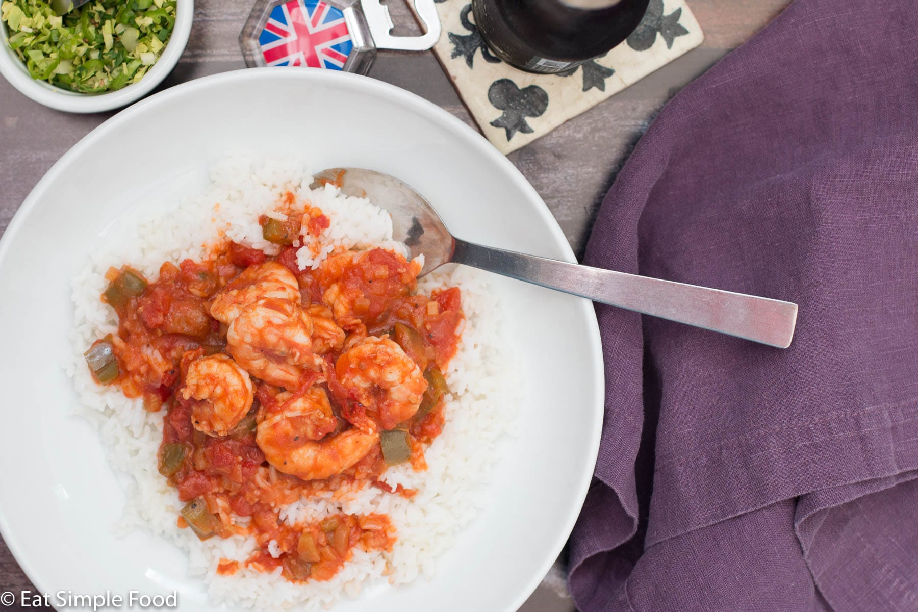 White bowl of shrimp in red tomato sauce over white rice and garnished with peppers and chopped celery leaves. Top view.
