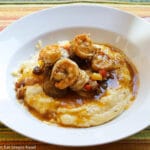 Shrimp In A Dark Roux With red and yellow peppers on yellow grits on a white plate.