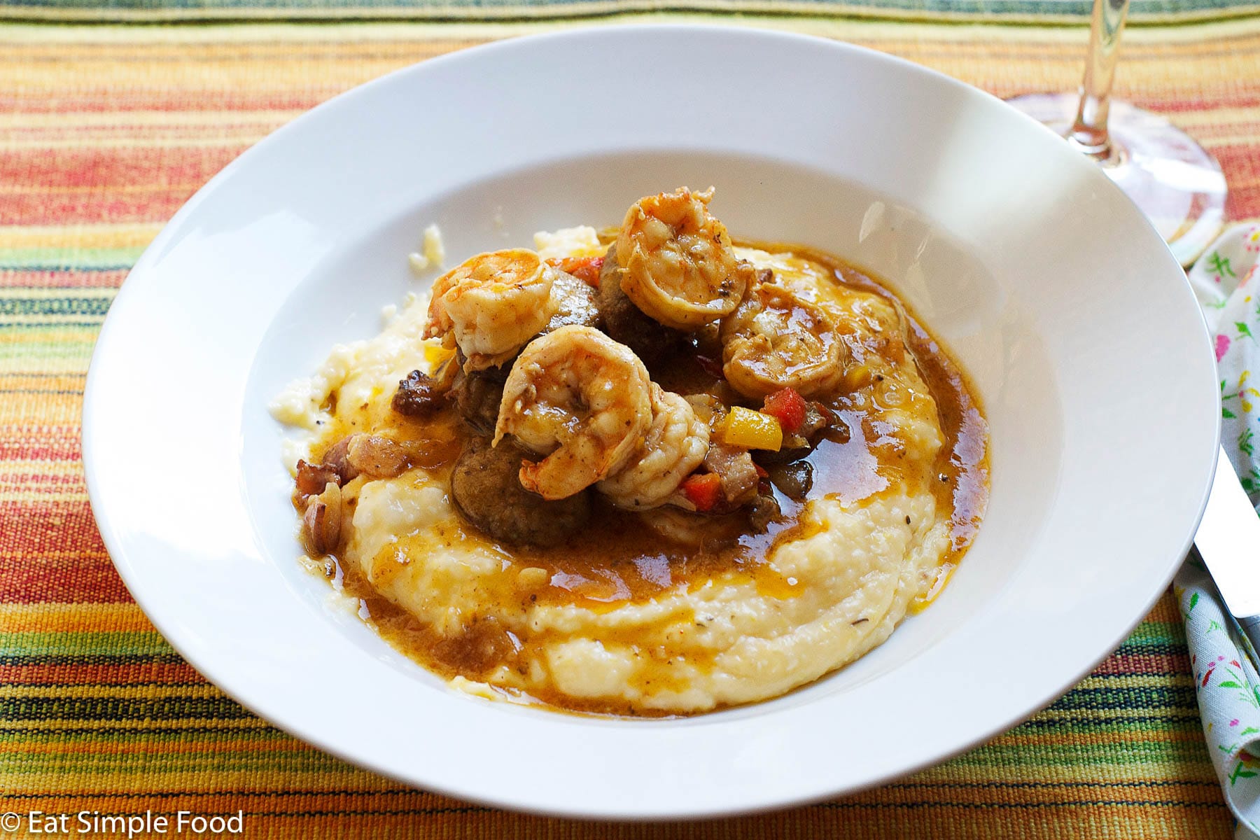 Shrimp In A Dark Roux With red and yellow peppers on yellow grits on a white plate.