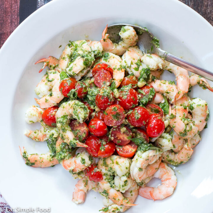 Cooked shrimp in a deep plate with halved cherry tomatoes and basil pesto. Garnished with Pine nuts.