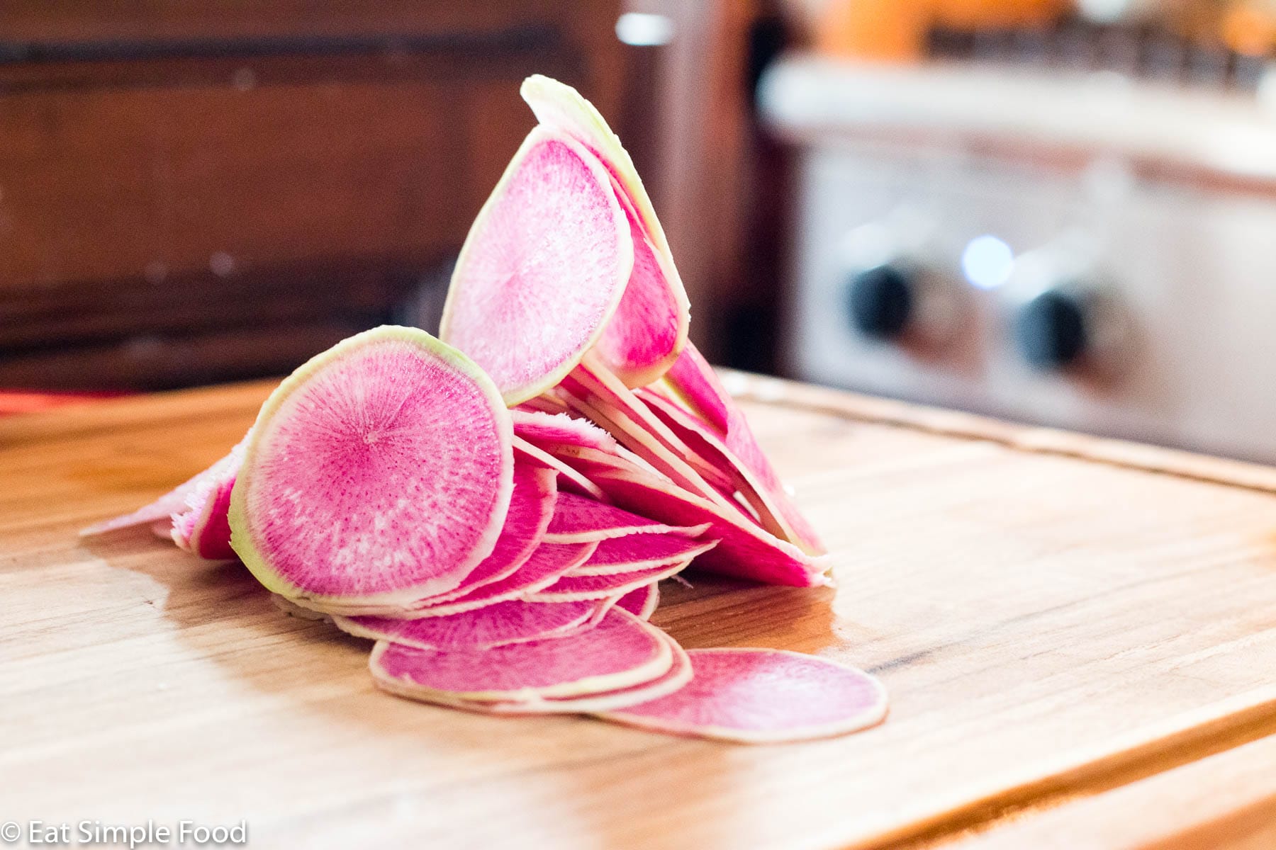 Sliced and vertically stacked pink and green watermelon radishes on a wood cutting board