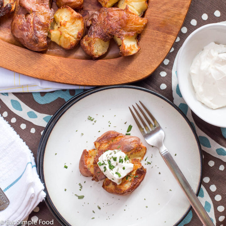 Top view of a smashed (flattened) potato with sour cream and chives. On a white plate with black rim.