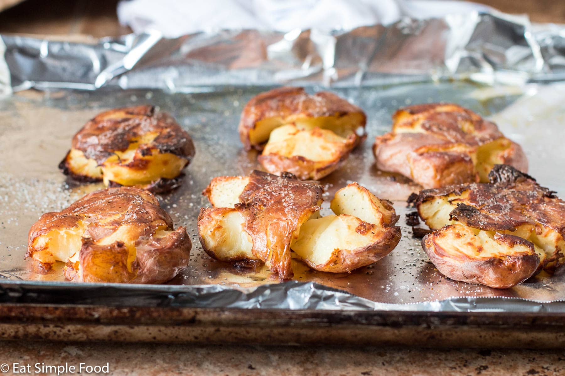 6 crispy smashed (flattened) potatoes on a sheet pan lined with aluminum foil