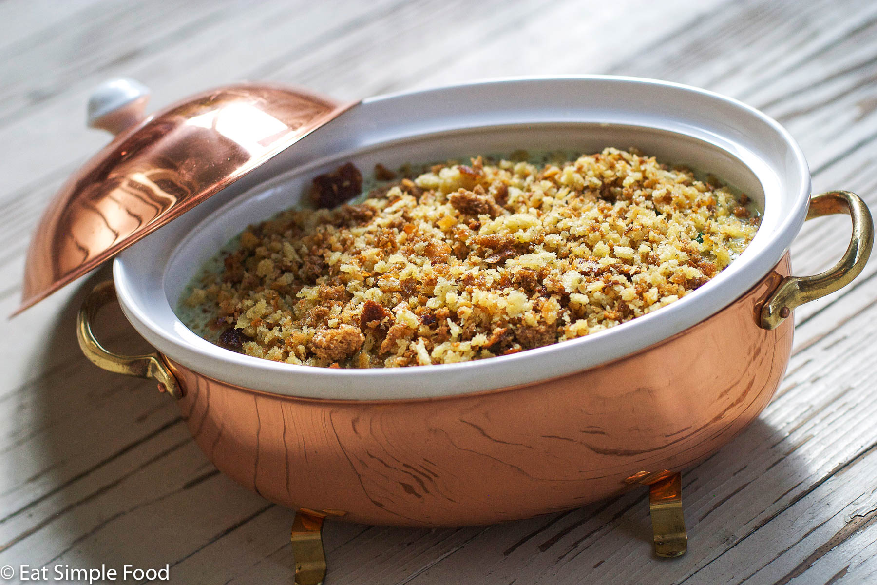 Spinach Gratin with a Crunchy breaded topping in a copper baking pan on a wood floor.