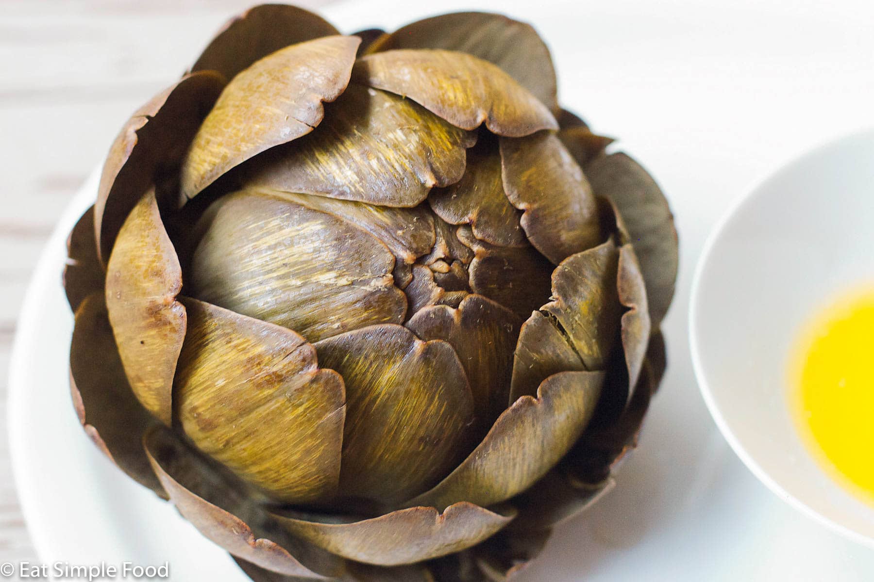 Whole Steamed Dark Green Artichoke Close Up on a White Plate. Top view.