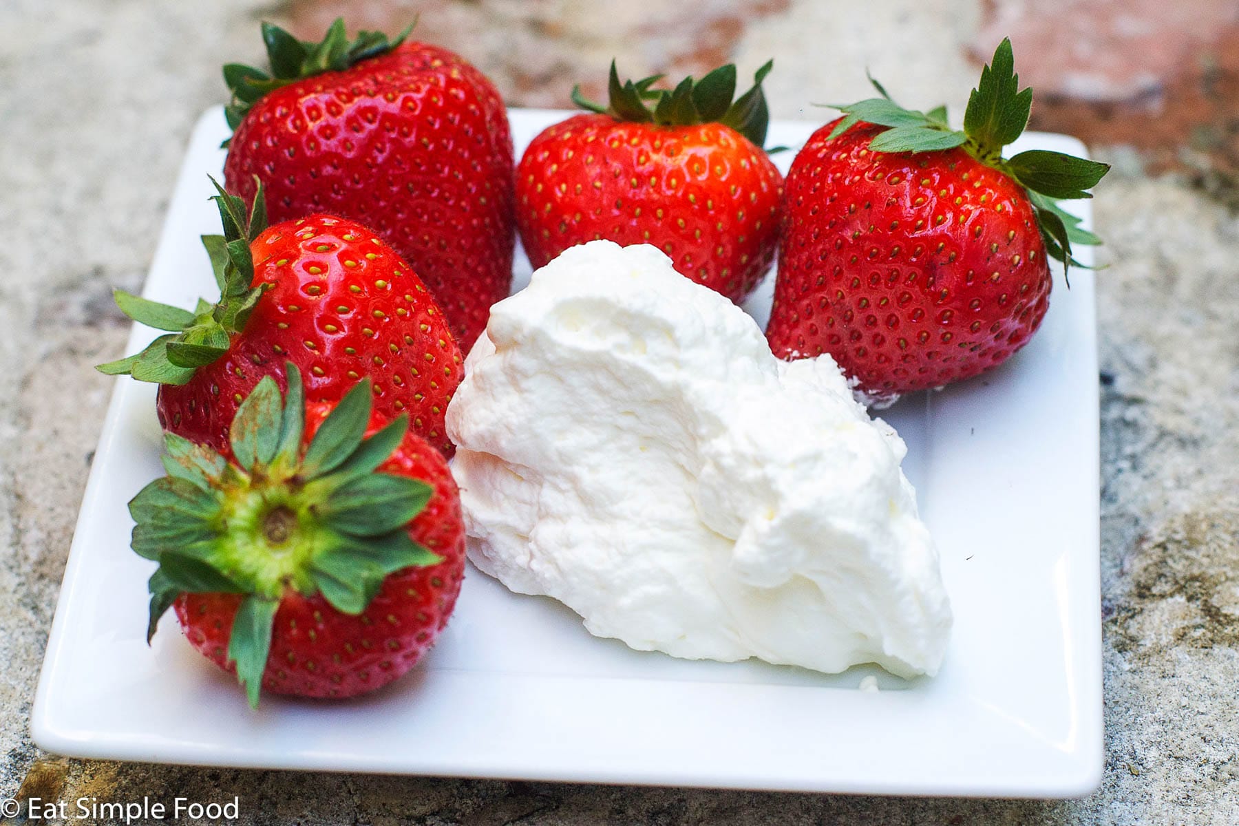 5 ripe strawberries on a small rectangle plate with a dollop of whipped cream.