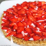 Side view of fresh sliced strawberry over a pink cream filling of a crispy tart.