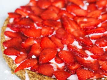 Side view of fresh sliced strawberry over a pink cream filling of a crispy tart.