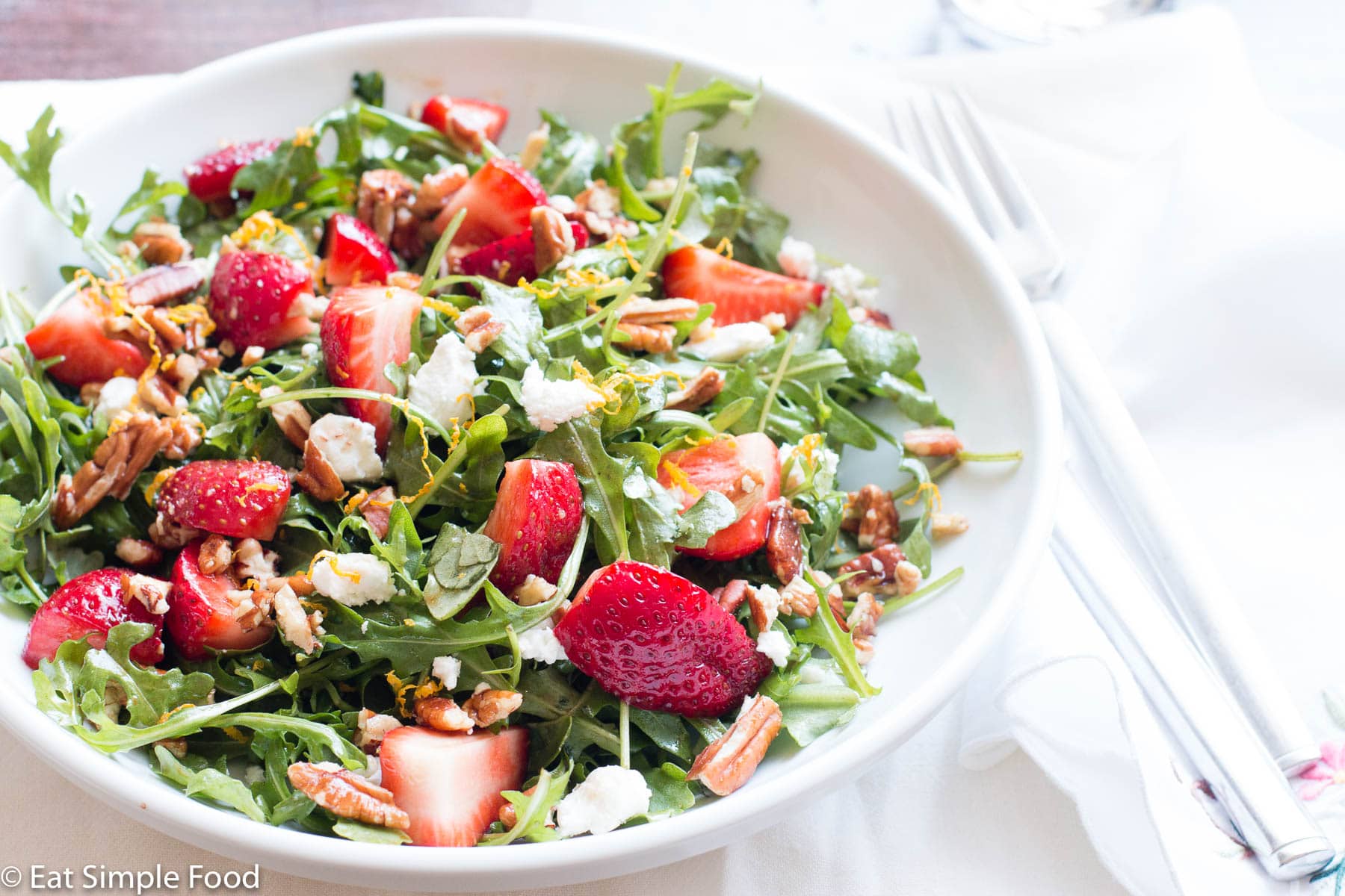 quartered strawberries, chopped pecans, and crumbled goat cheese on arugula salad on a shallow bowl/plate.