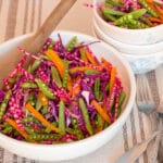 Close up. Bowl of sliced sugar snap peas, orange peppers, red cabbage, and candy stripe beet . Large White bowl with a wooden spoon.