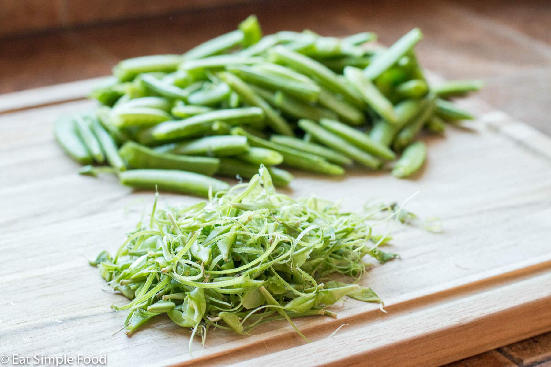 Sugar Snap Peas with fibrous veins removed on a wood cutting board. Side angle.