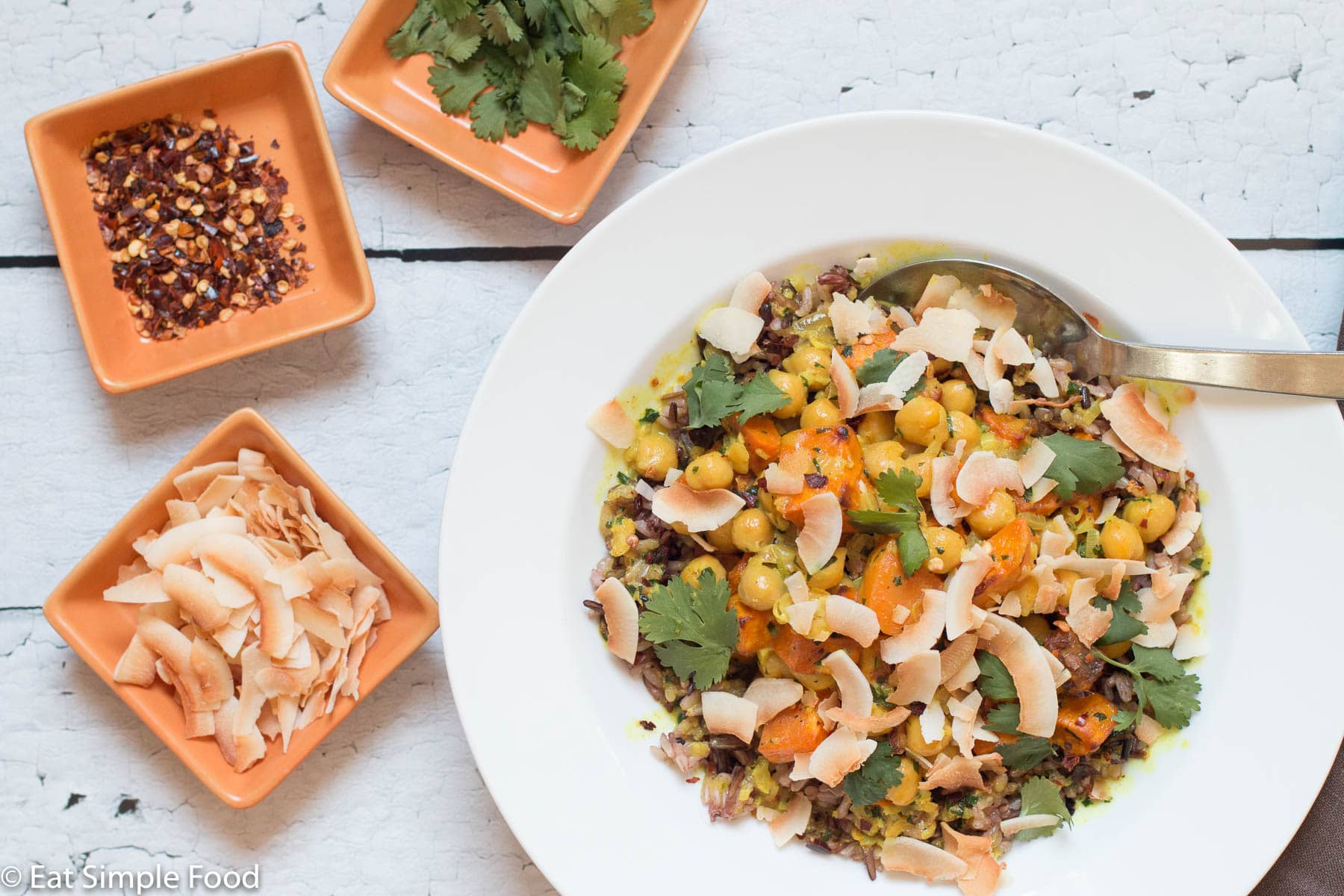 Top view of ¾ white deep plate with wild rice, chunks of roast sweet potatoes and chickpeas. Topped with cilantro and toasted coconut flakes.