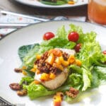2 plates of swordfish garnished with chunks of peach and pecan salsa over a bed of romaine lettuce with cherry tomatoes. Close up.