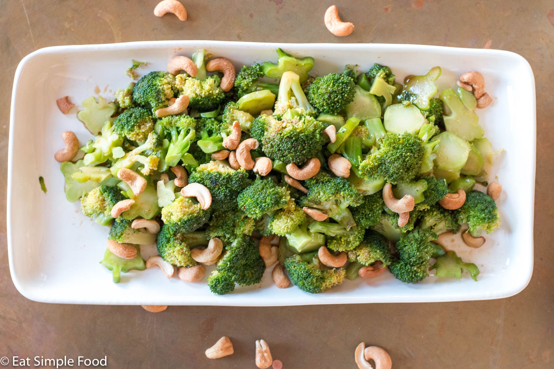 Broccoli w/ Tamari (Soy Sauce) & Cashews on a rectangle white plate on a copper table.