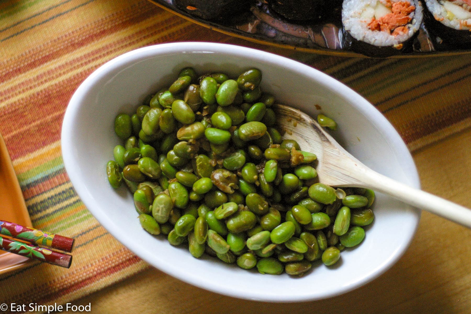 A Small white bowl filled with shelled edamame with a ginger and soy sauce. Top view with wooden spoon sticking out of bowl.