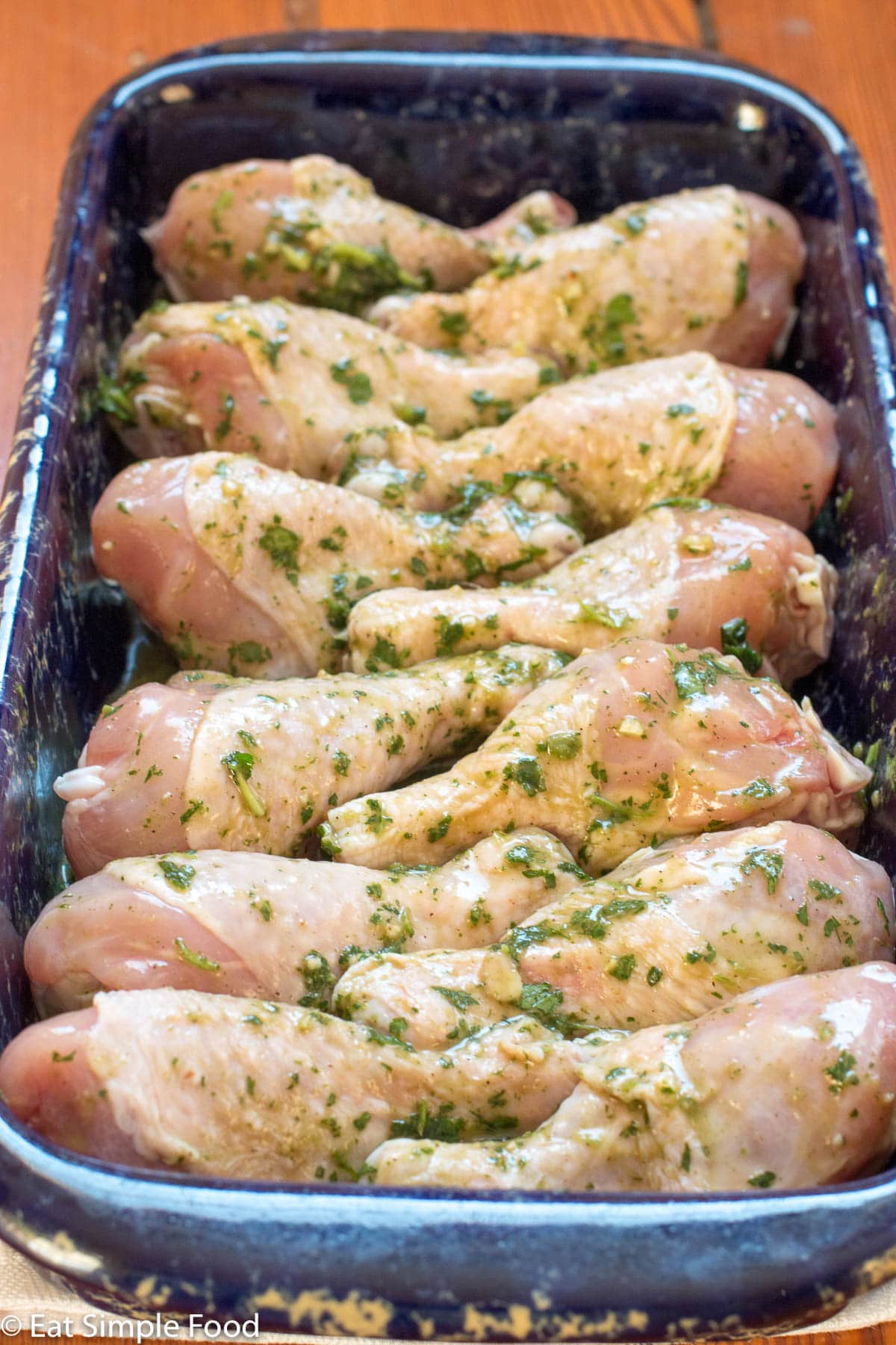 Uncooked Chicken legs in a cilantro sauce in a blue baking dish.