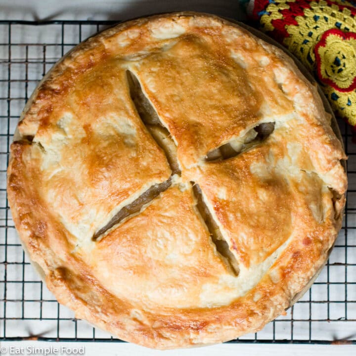 Top view of homemade apple pie on white table on a wire rack with a colorful hot pad in the background.