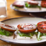 Layered sliced feta on the bottom and then arugula and topped with ripe red tomato. 2 small plates. 3 stacks on each plate.