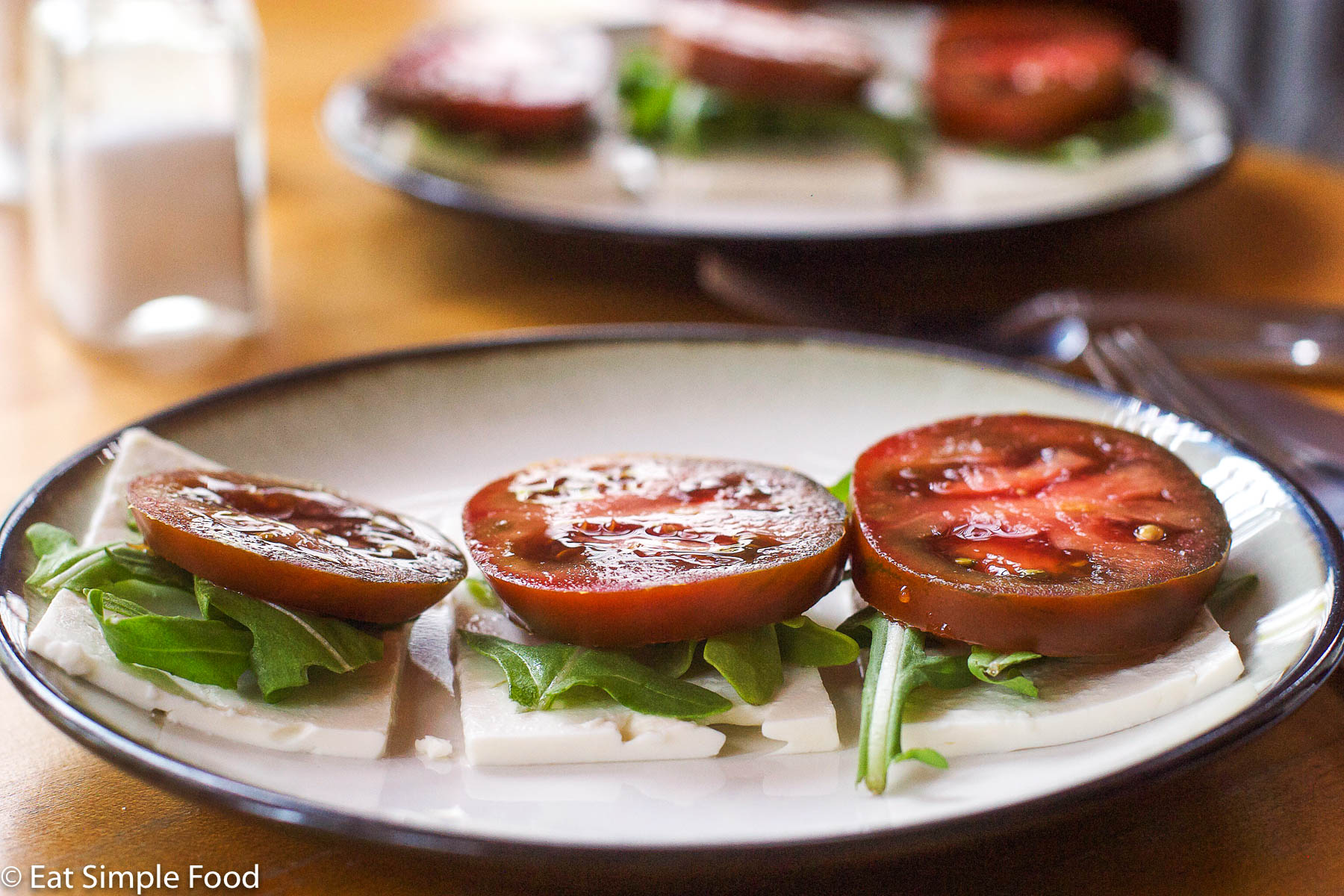 Layered sliced feta on the bottom and then arugula and topped with ripe red tomato. 2 small plates. 3 stacks on each plate.