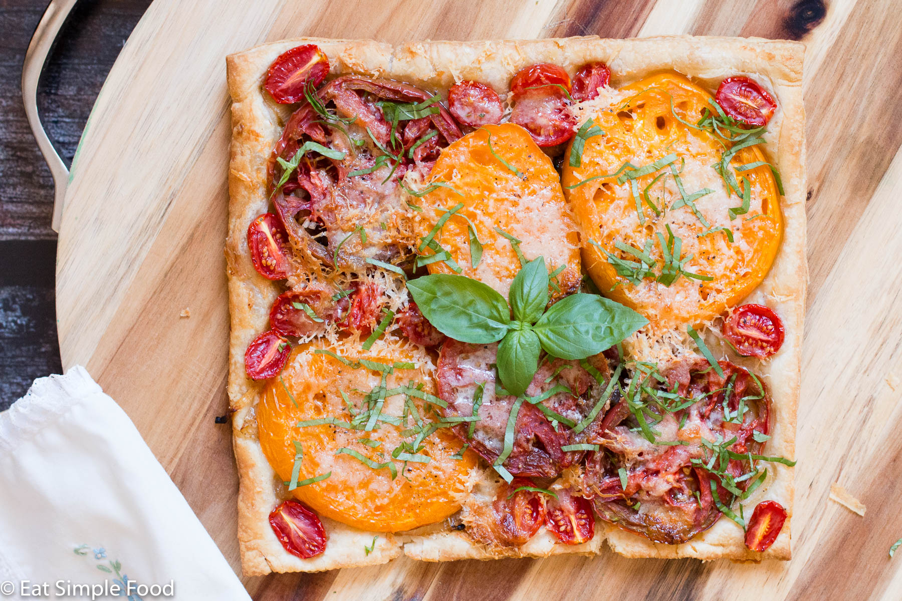 Tomato Tart with different sizes and colors of tomatoes on golden puff pastry with basil leaves and sliced basil garnish.