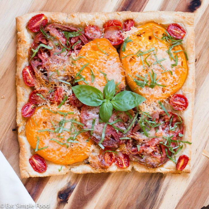 Tomato Tart with different sizes and colors of tomatoes on golden puff pastry with basil leaves and sliced basil garnish.