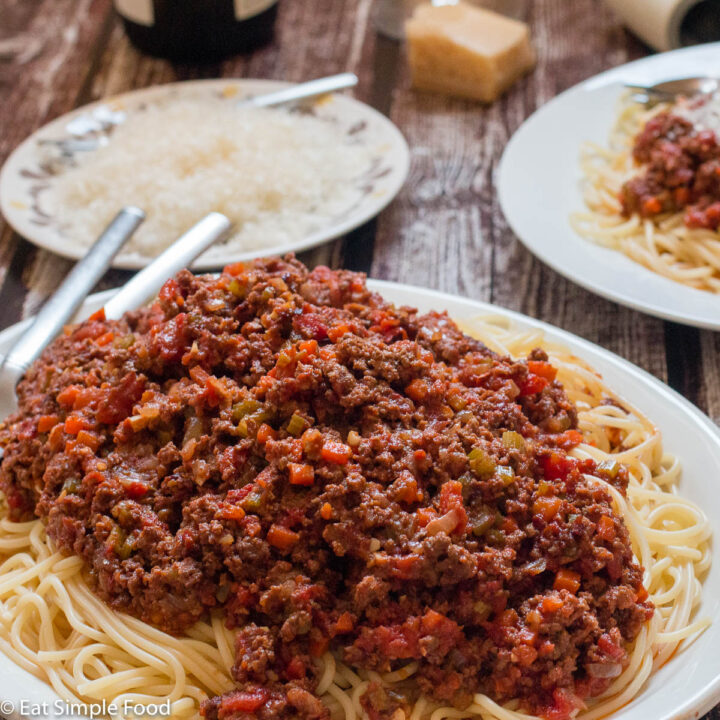 Beef Bolognese on a white plate with a plate . Close up. Parmesan Cheese garnish on plate in background.