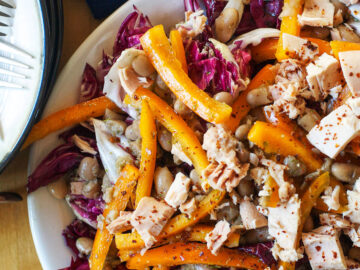 Purple Radicchio, sliced orange bell peppers, chunks of albacore white tuna, and white beans in a white large shallow plate with a fork.