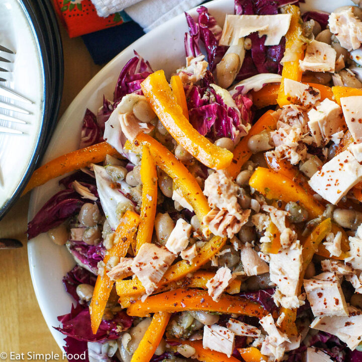 Purple Radicchio, sliced orange bell peppers, chunks of albacore white tuna, and white beans in a white large shallow plate with a fork.