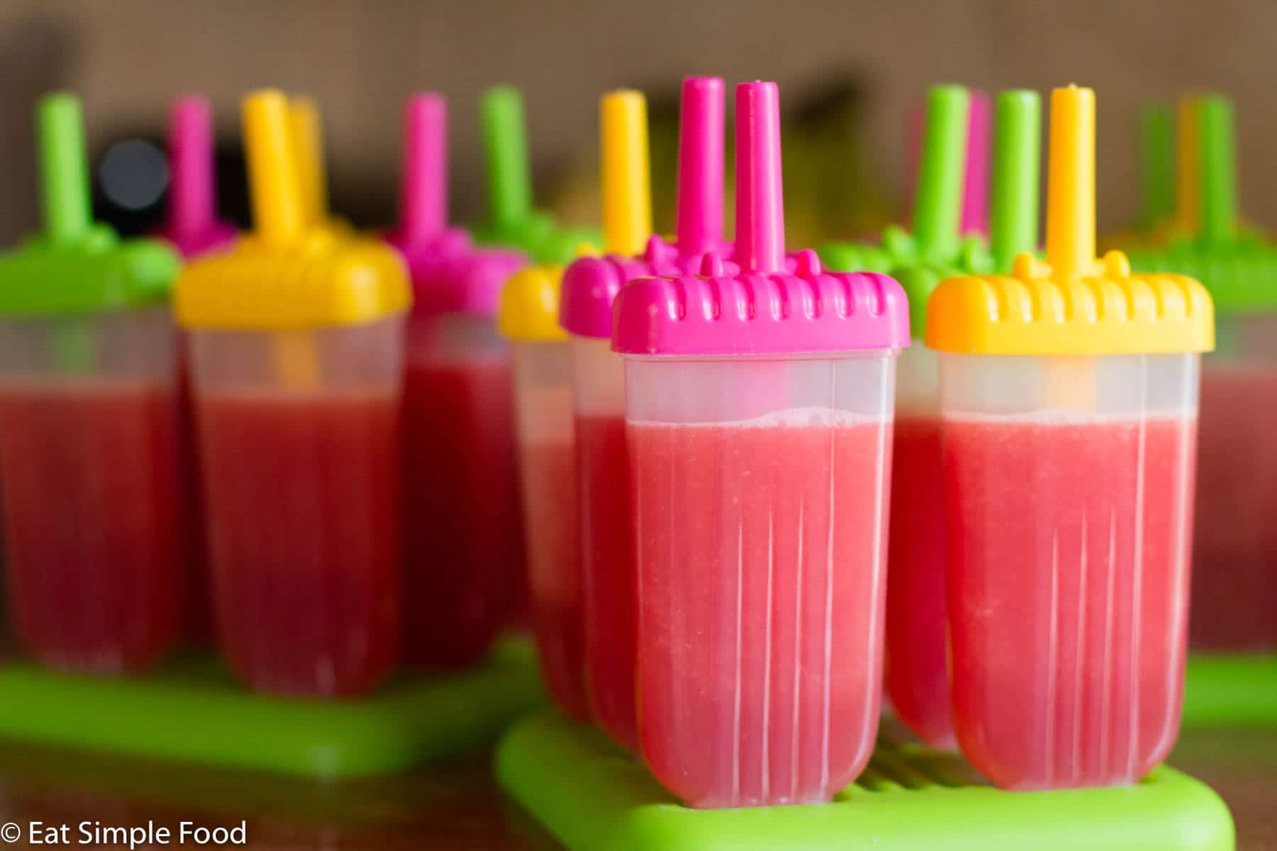 Pink Watermelon Popsicles in plastic molds with coloful tops. Around 14 popsicles.