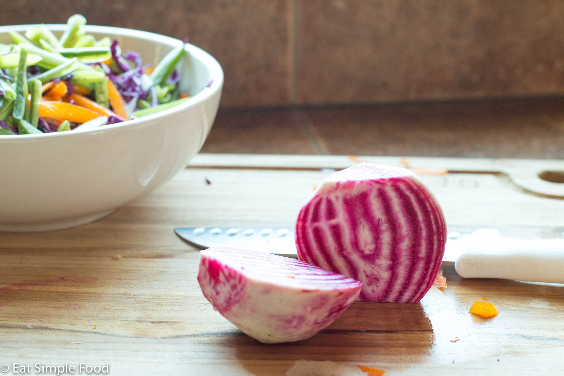 Candy striped Watermelon Radish peeled and cut in half on wood cutting board with chef's knife in background.