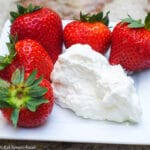 5 ripe strawberries on a small rectangle plate with a dollop of whipped cream.