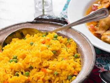 Yellow Spanish Rice With Peas and Carrots In a Brown Bowl With a spoon On a Dark Wood Table.