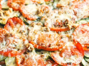 Close up of Zucchini & Tomato Casserole in an oval white baking dish. Parmesan melted on top with chopped walnuts.