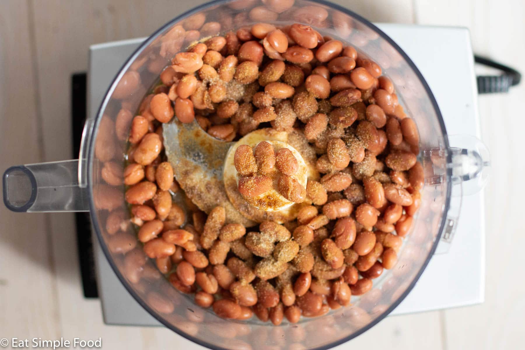 Top view of food processor filled with drained pinto beans and spices.