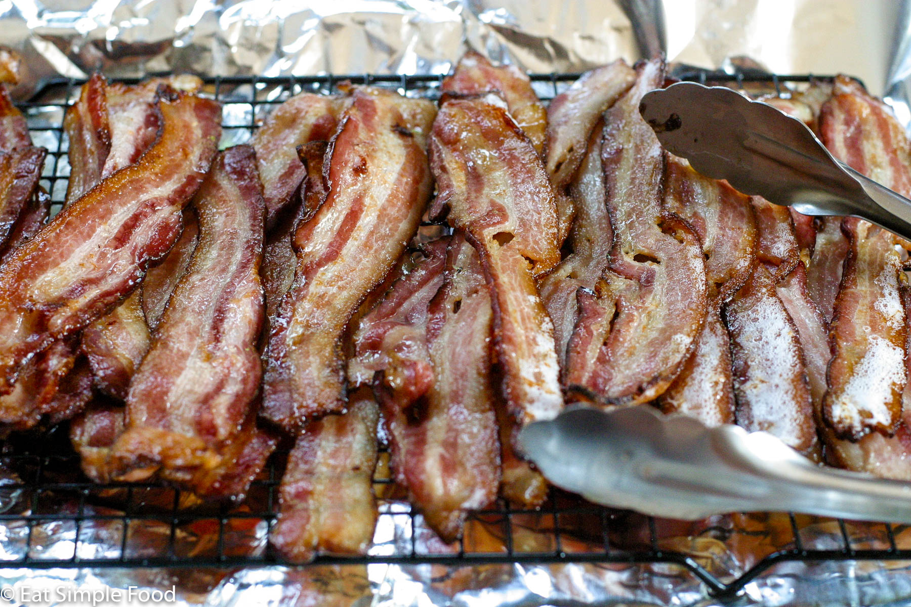 Brown Roasted Crispy bacon on an elevated wire rack over an aluminum lined sheet pan. Side view.